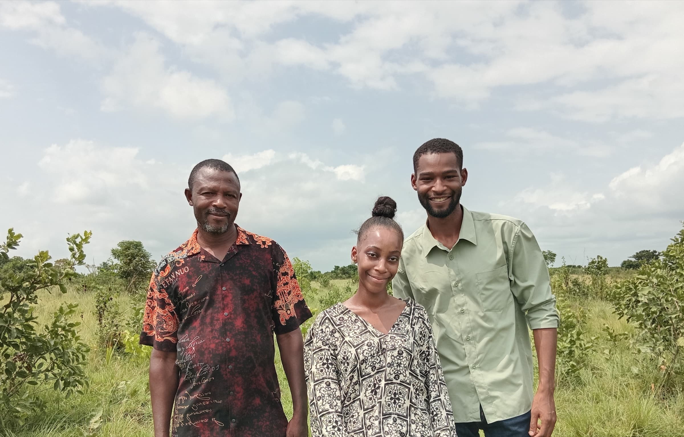 Three people, including Ubuntu Eco Gardens founder Kayode Ewuoso, standing together in the open grassland at the development site
