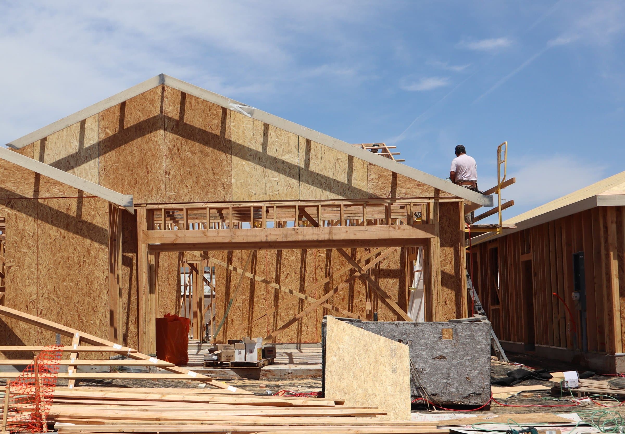 A home under construction, framed in timber against a clear blue sky